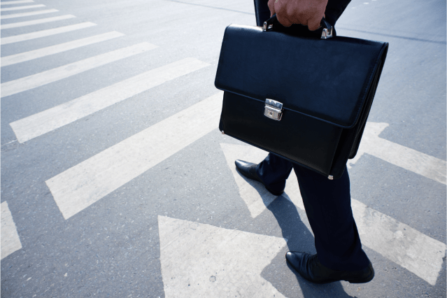 A stock image of a person carrying a briefcase and walking through an intersection.