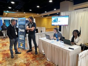 SnapStream’s Brennan Murphy and Alexia Awoseyi monitor and clip a live panel discussion while Matt Quering, head of sales, speaks to a conference attendee at the company’s Midway booth during ONA23.